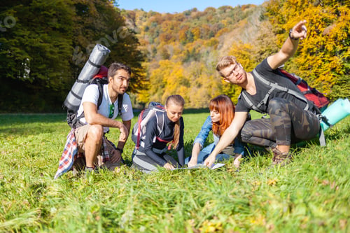 Preview: Group of hikers with backpacks looking at map and planning further trekking trail