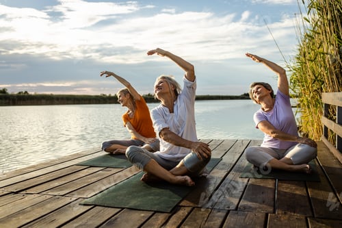 Preview: Group of senior woman doing yoga exercises by the lake.