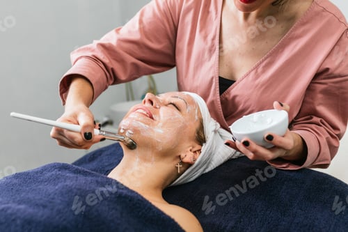 Preview: Anonymous professional beautician applying facial mask on face of client