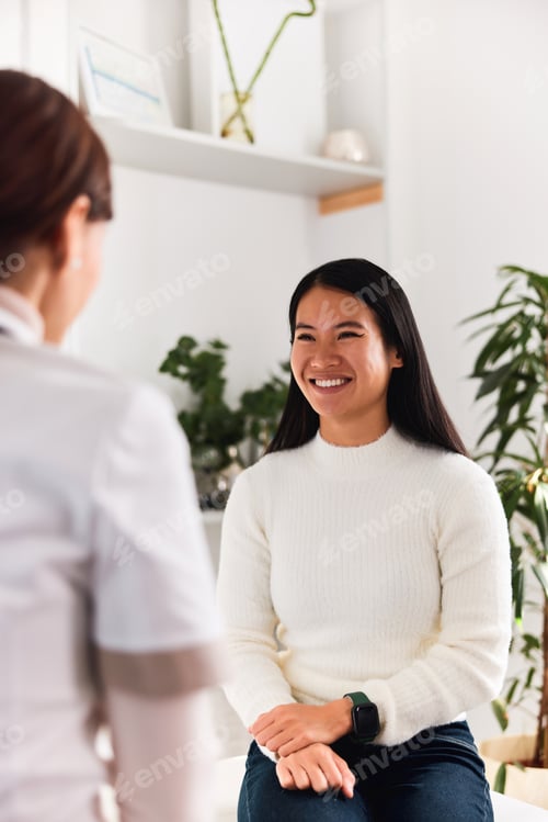 Preview: A happy Asian female patient talking with a female dermatologist at the clinic.
