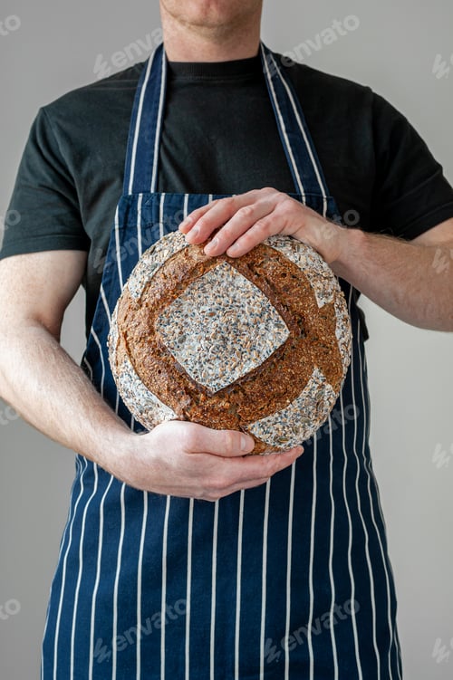 Preview: Close-up at bakers hands holding a loaf of bread in front of him.