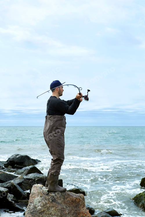 Preview: Young man on rock casting fishing rod to sea