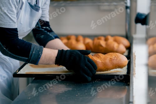 Preview: close-up of a baker's hands in professional kitchen taking bread from a tray