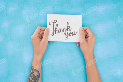 Preview: cropped person holding paper with thank you lettering isolated on blue background