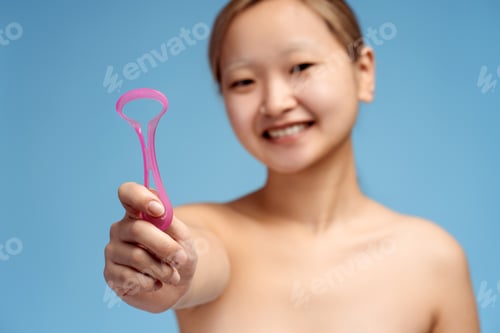 Preview: Happy Asian girl holding device for hygienic cleaning for tongue, isolated on blue