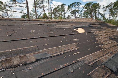 Preview: Wind damaged house roof with missing asphalt shingles after hurricane Ian in Florida.