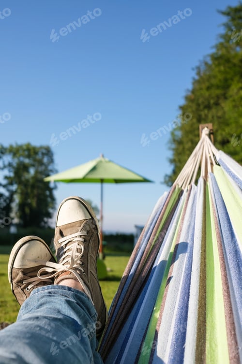 Preview: Male legs in sneakers and jeans in a hammock, on a warm summer day, camping. Lifestyle.