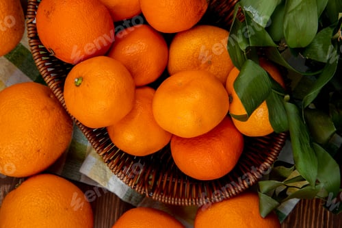 Preview: top view of fresh ripe oranges in a wicker basket on plaid tablecloth