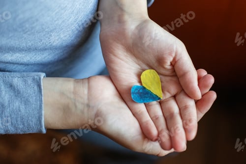 Preview: Heart of yellow-blue colors of national flag of Ukraine in childs hand. Top view. Stop War.