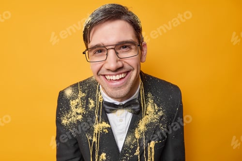 Preview: Positive birthday man wears formal suit and transparent glasses smeared with serpantine spray has fe