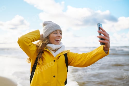 Preview: Tourist with phone. Selfie time. Tourist in yellow jacket posing by sea at sunset. Travelling.