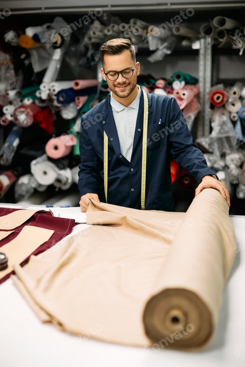 Preview: Happy textile worker using roll of fabric while working at tailor's workshop.