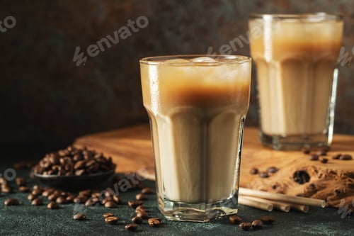 Preview: Ice coffee in a tall glass with cream poured over, ice cubes and beans on a dark concrete table.