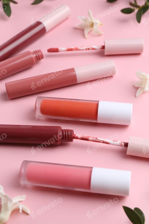 Preview: Different lip glosses, applicators, flowers and green leaves on pink background