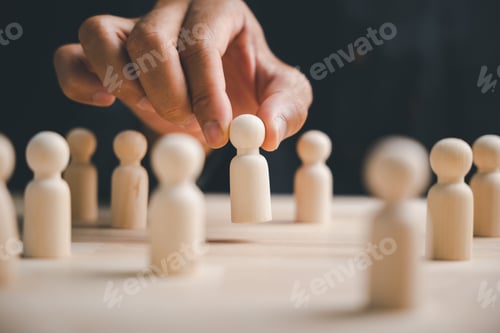 Preview: Hand picking out a wooden figure from a row of figures on a table, representing a choice or