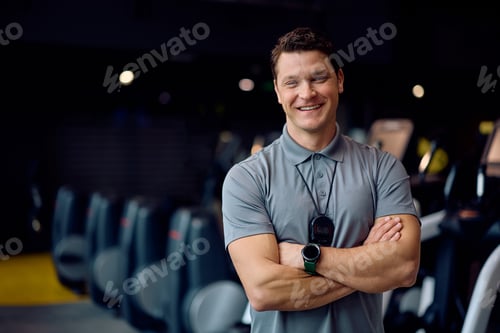 Preview: Confident personal trainer with crossed arms in a gym looking at camera.