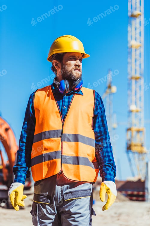 Preview: Young builder in reflective vest and hardhat standing at construction site