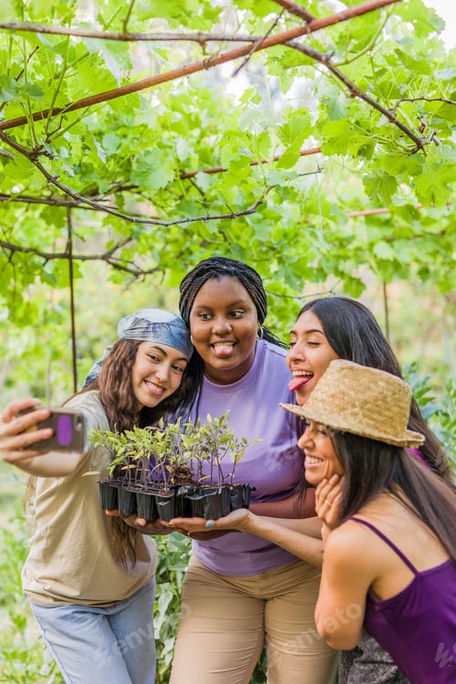 Preview: Multiethnic volunteer group selfie. Friendship teamwork in urban garden. Latin and Moroccan women