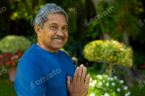Preview: Senior man standing in lush backyard garden smiling and holding hands in greeting gesture