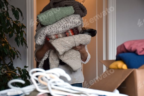 Preview: Woman holding a huge stack of winter knit sweaters, organizing and sorting clothes in her closet