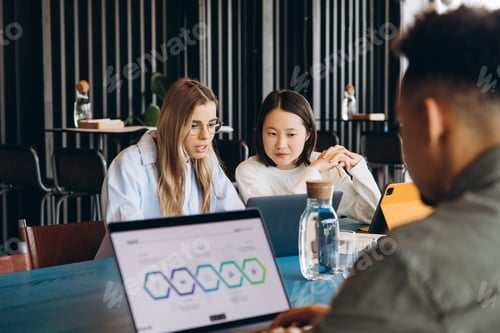 Preview: Focused diverse team collaborating on project using laptops in modern office