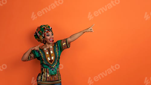 Preview: Excited african lady in colorful outwear pointing at copy space