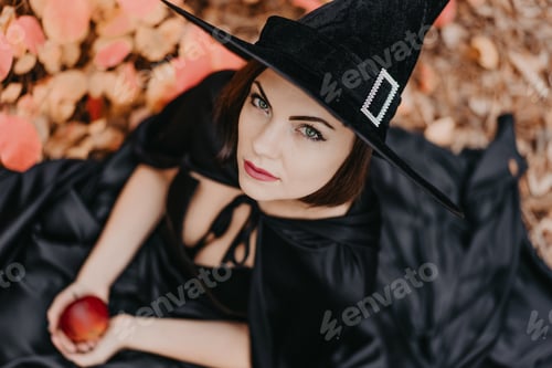 Preview: Portrait of woman as witch in black holding red apple as symbol of temptation, poison