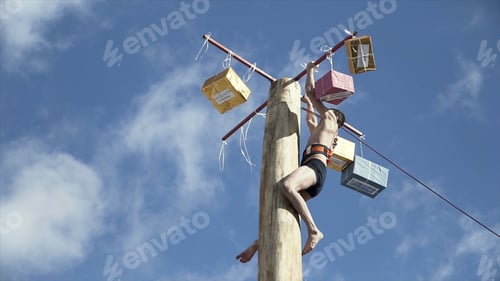Preview: Bottom view of a young man at the top of a wooden pole trying to get the prize, traditional holiday