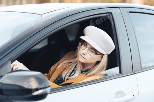 Preview: Middle-aged woman driver driving a car. Pretty female with hat and glasses, transport concept