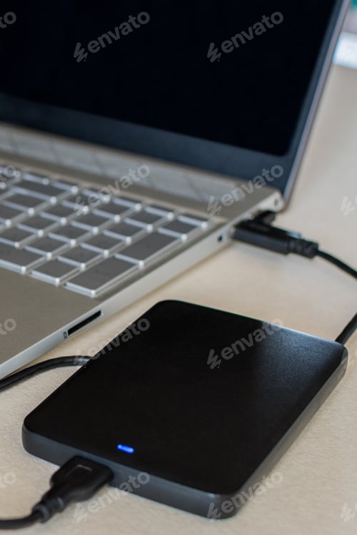Preview: External hard drive connected to a laptop computer on a desk. A portable hard drive