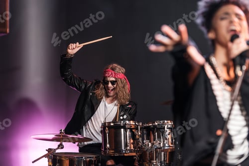 Preview: Smiling young man playing drums set with singer on stage