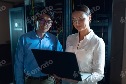 Preview: Diverse male and female engineers using laptop in computer server room