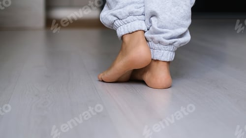 Preview: Close up of barefoot young female walking on warm heated wooden floor at home.