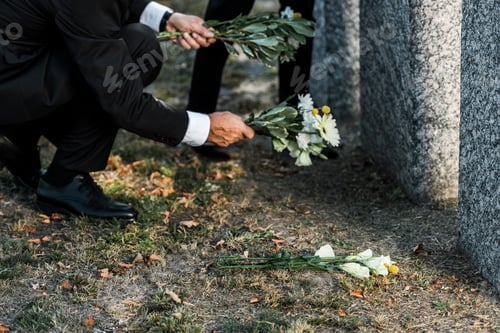 Preview: cropped view of senior man putting flowers near tombs