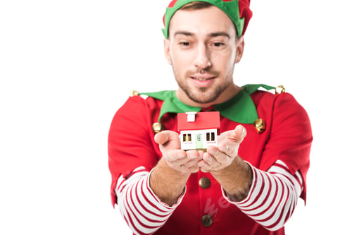 Preview: man in christmas elf costume holding house model isolated on white, real estate sale and insurance