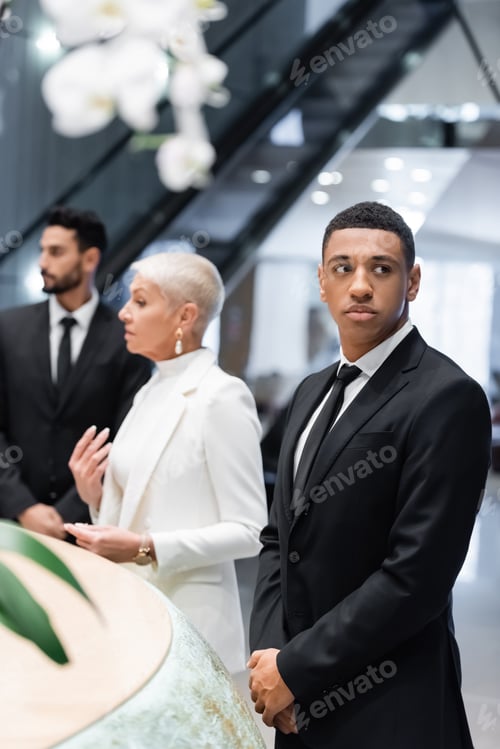 Preview: multiethnic bodyguards protecting mature businesswoman checking in at hotel reception