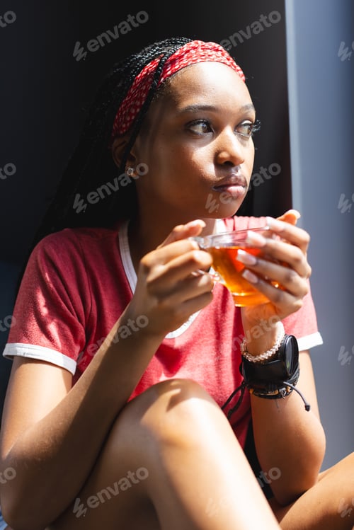 Preview: A young African American woman enjoys a cup of tea, gazing thoughtfully