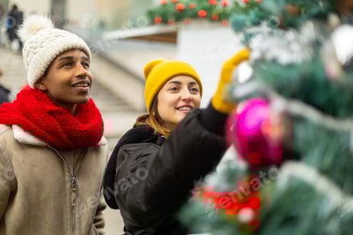Preview: Young couple decorating christmas tree outdoors at christmas market