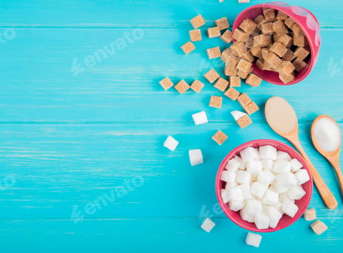 Preview: top view of white and brown sugar cubes in bowls on blue wooden background with copy space