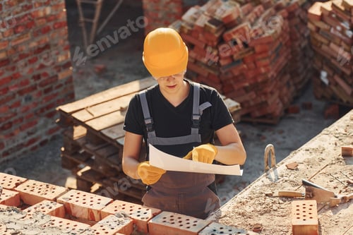 Preview: Holding plan in hands. Construction worker in uniform and safety equipment have job on building
