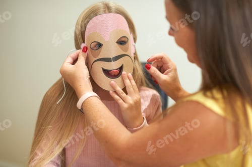 Preview: Mother attaching paper mask to daughter's face