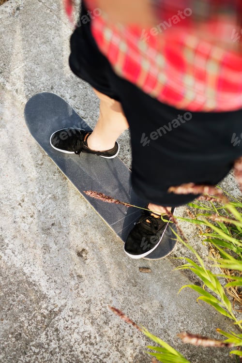Preview: High angle low section of young woman skateboarding on footpath
