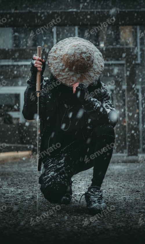 Preview: Vertical shot of a man with a Sword and Asian hat on his nee under the snow