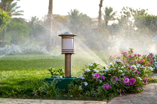 Preview: Plastic sprinkler irrigating flower bed on grass lawn with water in summer garden.