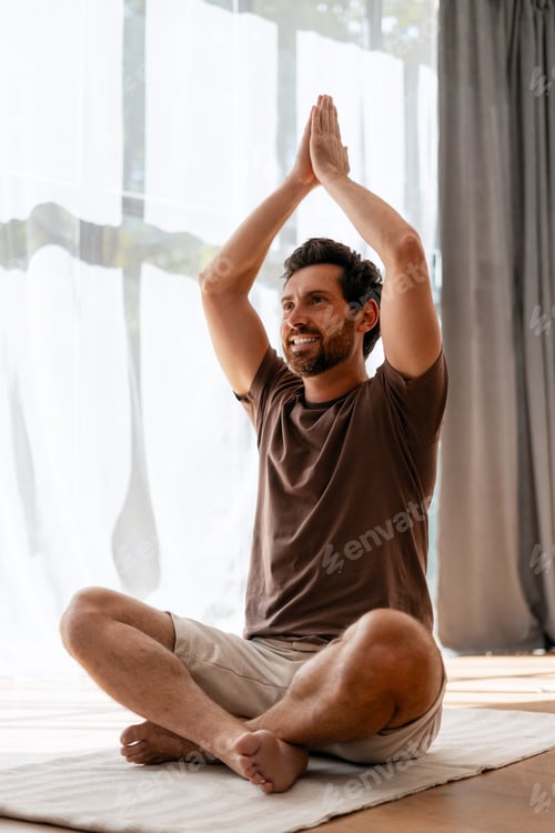 Preview: Man practicing yoga, meditating in lotus position with hands raised at home