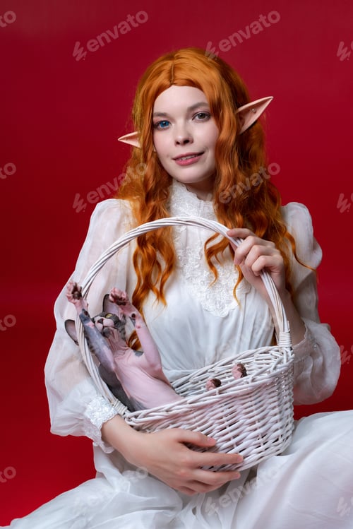 Preview: Redhead cosplayer elf young woman in white dress holds white wicker basket with Sphinx cat
