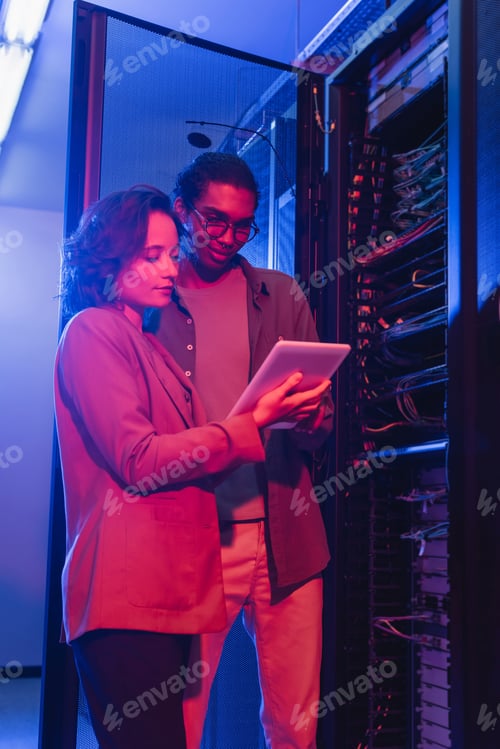 Preview: interracial engineers using digital tablet while checking server in data center