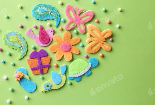 Preview: Different small colorful felt items and beads on green background, flat lay