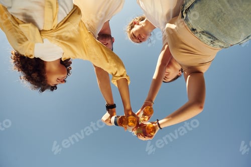 Preview: Upside down. View from below of people that are cheering with beer bottles