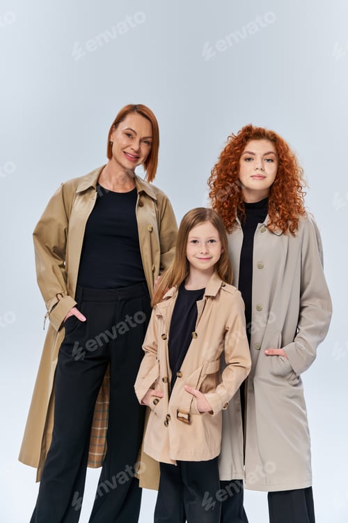 Preview: redhead girl posing near happy family in coats on grey backdrop, generations, hands in pockets